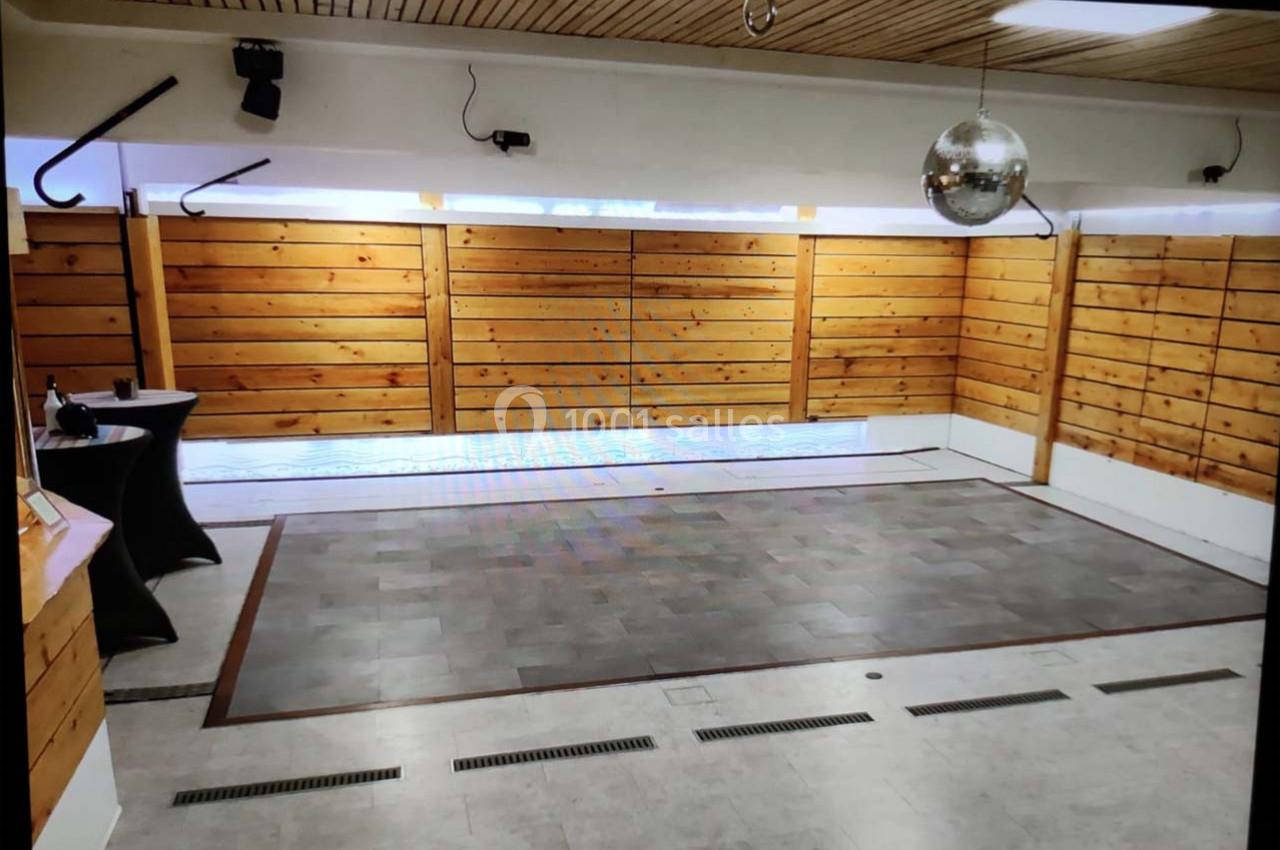 Salle avec parquet central, murs en bois, plafond en lambris, spots lumineux et boule disco suspendue.