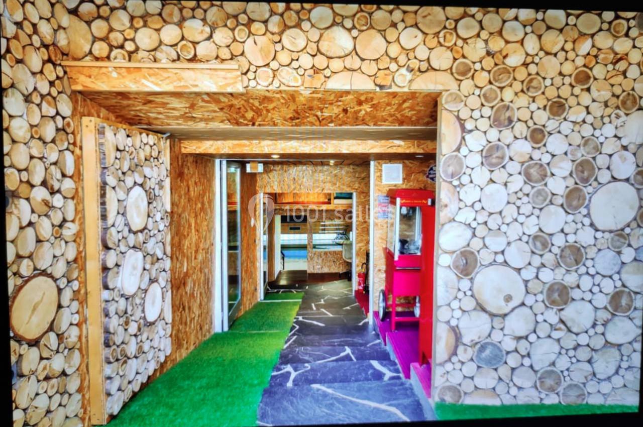 Mur en rondins de bois décoratifs, sol en pierre et gazon artificiel, avec des équipements modernes en arrière-plan.