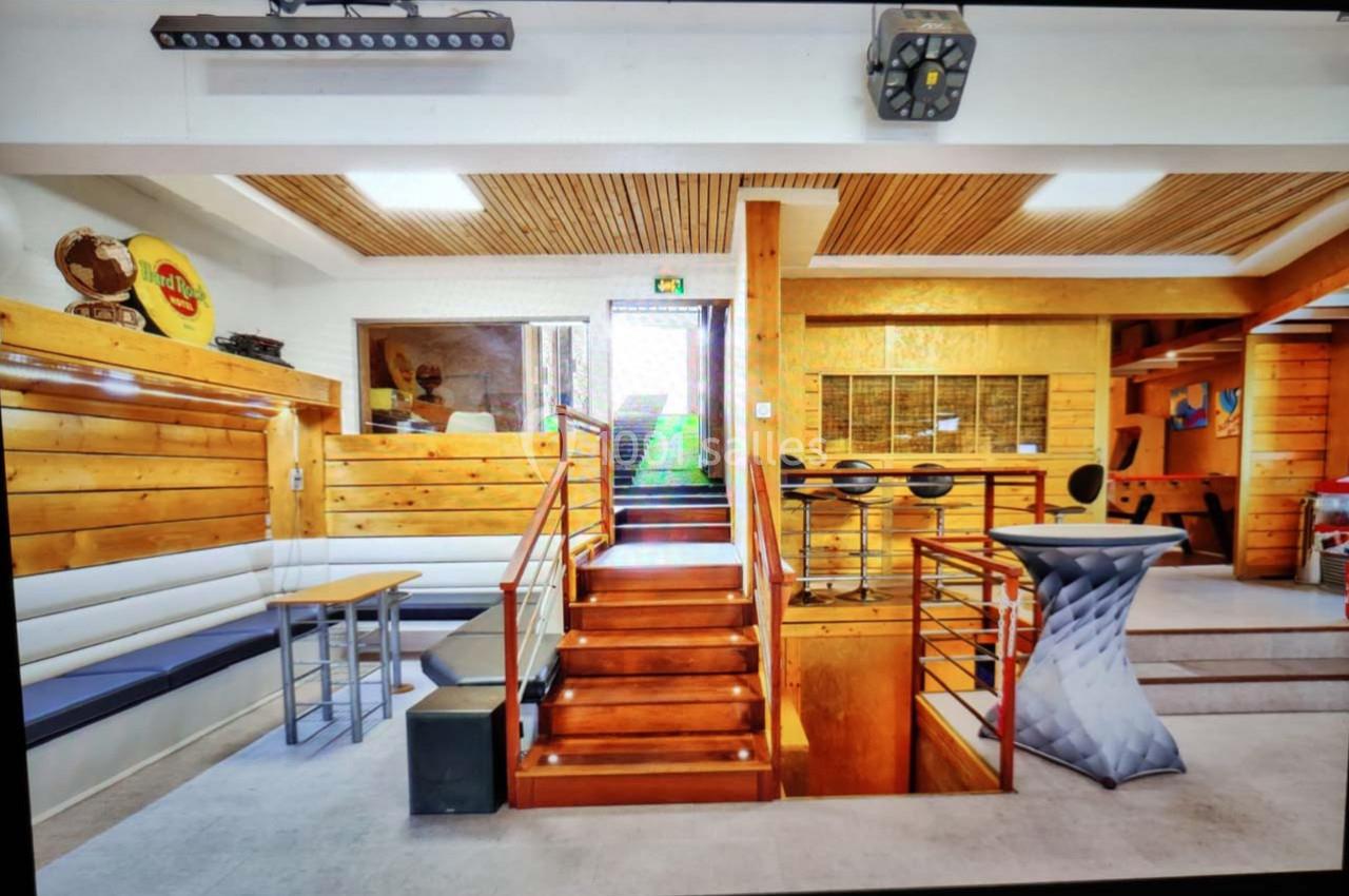 Intérieur d'un espace en bois avec escaliers, banquettes, tables hautes et éclairage moderne.