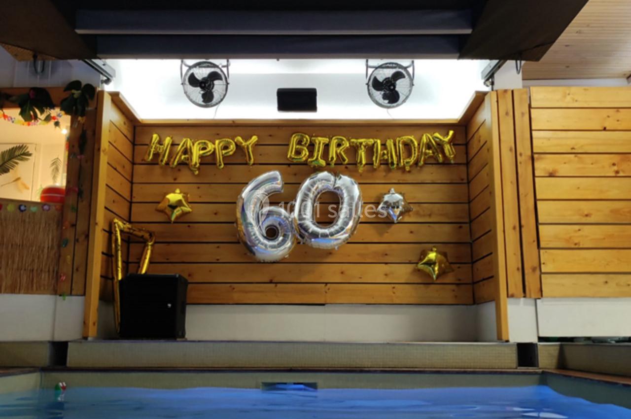 Décoration d'anniversaire avec des ballons dorés ’Happy Birthday’ et ’60’ au-dessus d'une piscine intérieure.