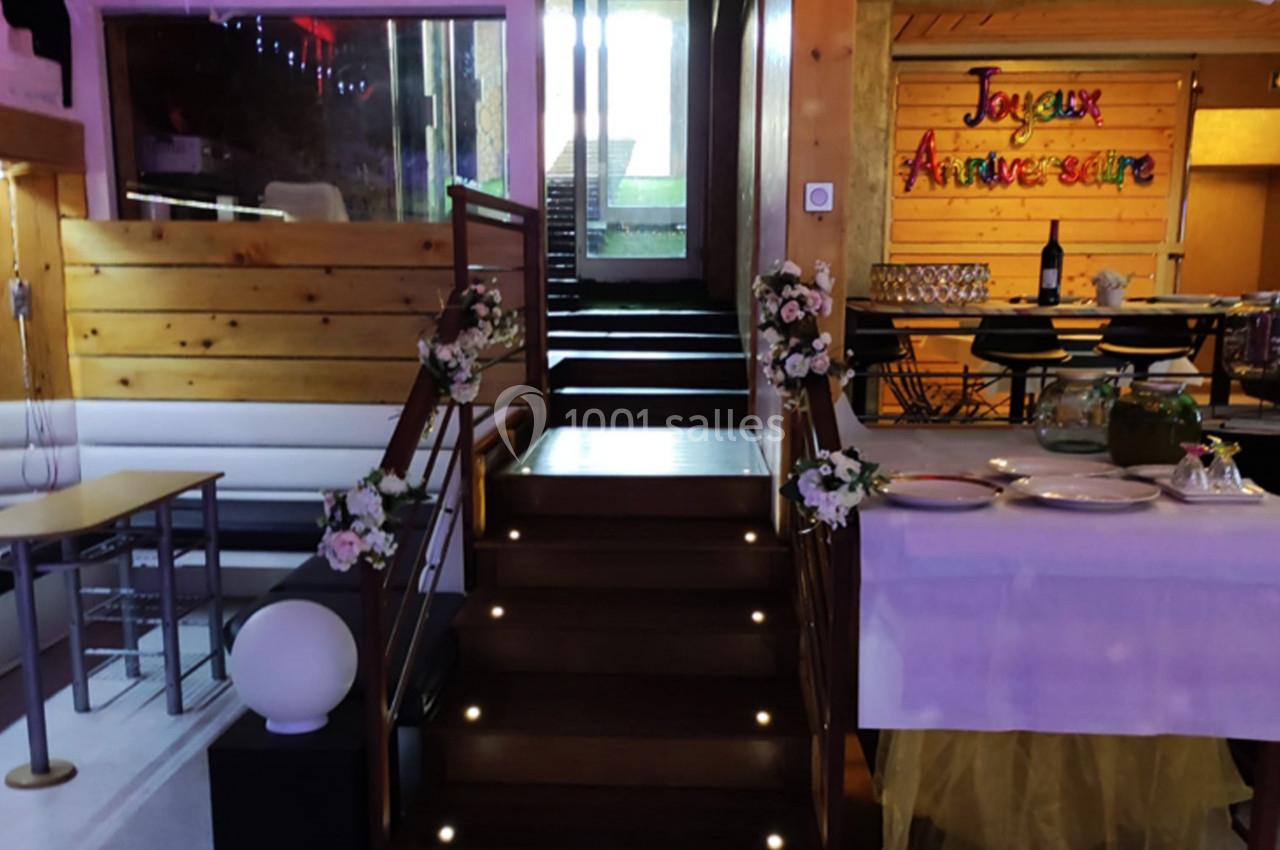 Escalier décoré de fleurs menant à une salle festive avec une table dressée et une bannière ’Joyeux Anniversaire’.