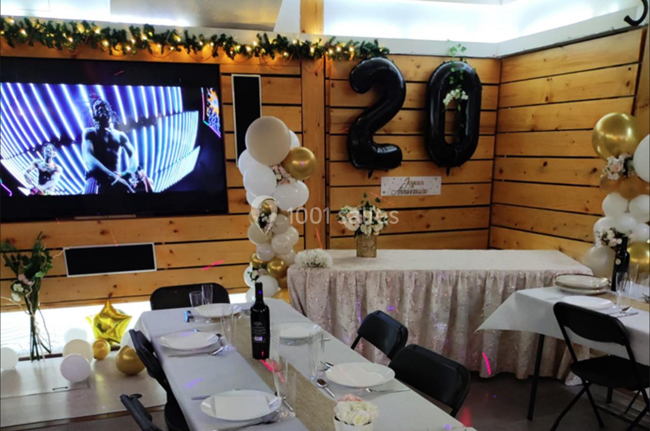 Salle décorée pour une fête avec ballons ’20’, table dressée et écran affichant une image lumineuse.