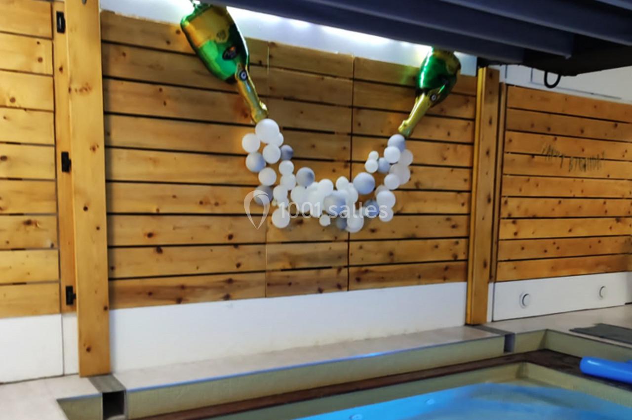 Décoration murale avec deux bouteilles factices de champagne et une guirlande de ballons blancs, près d'une piscine.