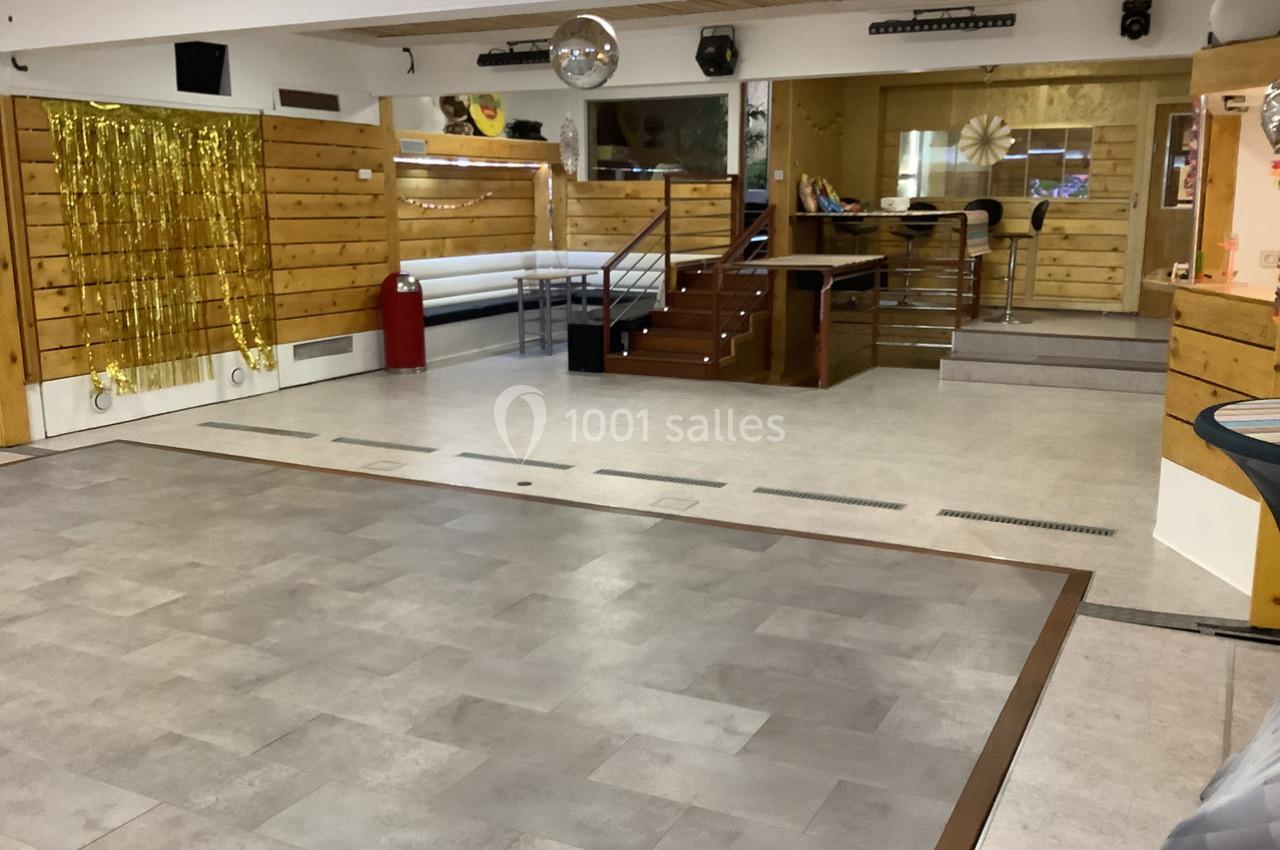 Salle vide avec parquet, murs en bois, décorations dorées et une boule disco suspendue au plafond.