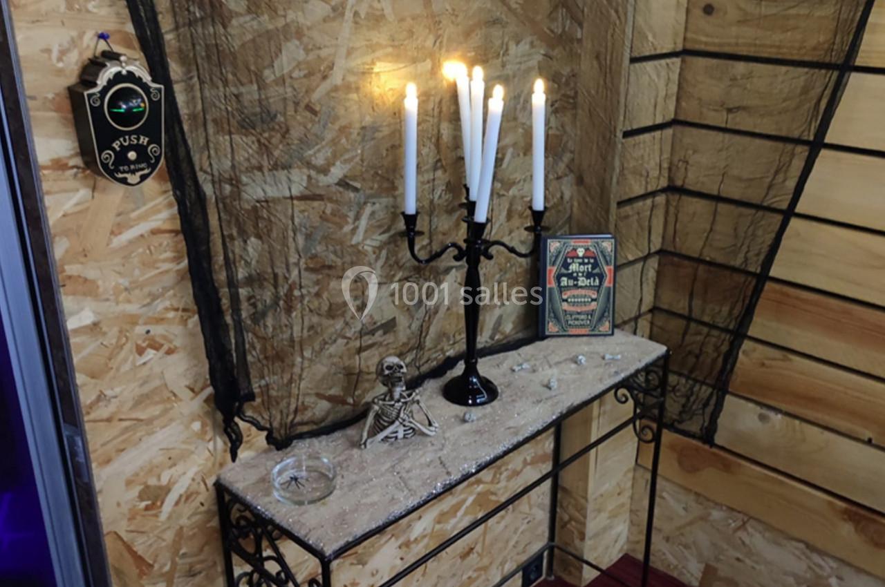 Chandelier allumé sur une console en métal avec un décor sombre, filet noir et squelette miniature.