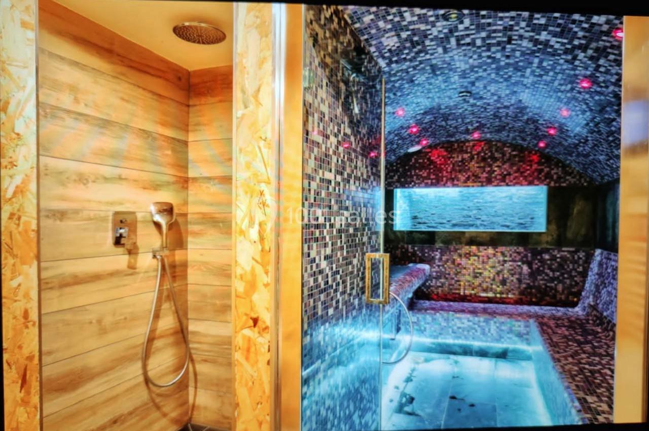 Douche moderne en bois clair à gauche et hammam carrelé avec éclairage tamisé à droite.