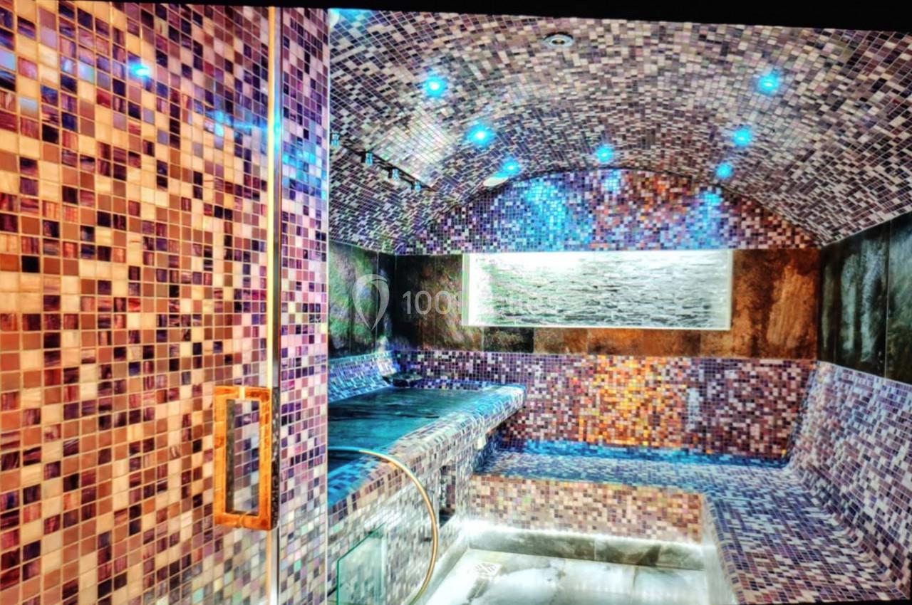 Hammam moderne avec murs et plafond en mosaïque colorée, éclairage tamisé et banc en pierre.