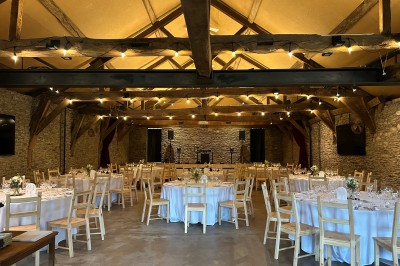 Chambre mansardée lumineuse avec poutres apparentes, lit double, baignoire, lavabo et poêle noir.