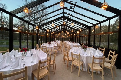 Chambre mansardée lumineuse avec poutres apparentes, lit double, baignoire, lavabo et poêle noir.