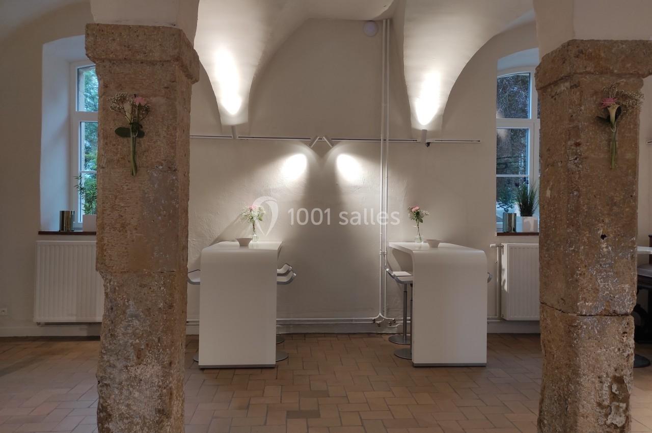 Deux colonnes en pierre encadrent un espace avec deux bureaux modernes, éclairés par des lampes murales.