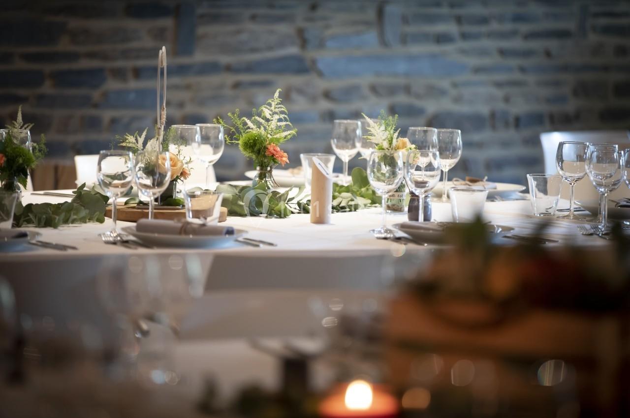 Table élégamment dressée avec des verres, assiettes et décorations florales sur fond de mur en pierre.