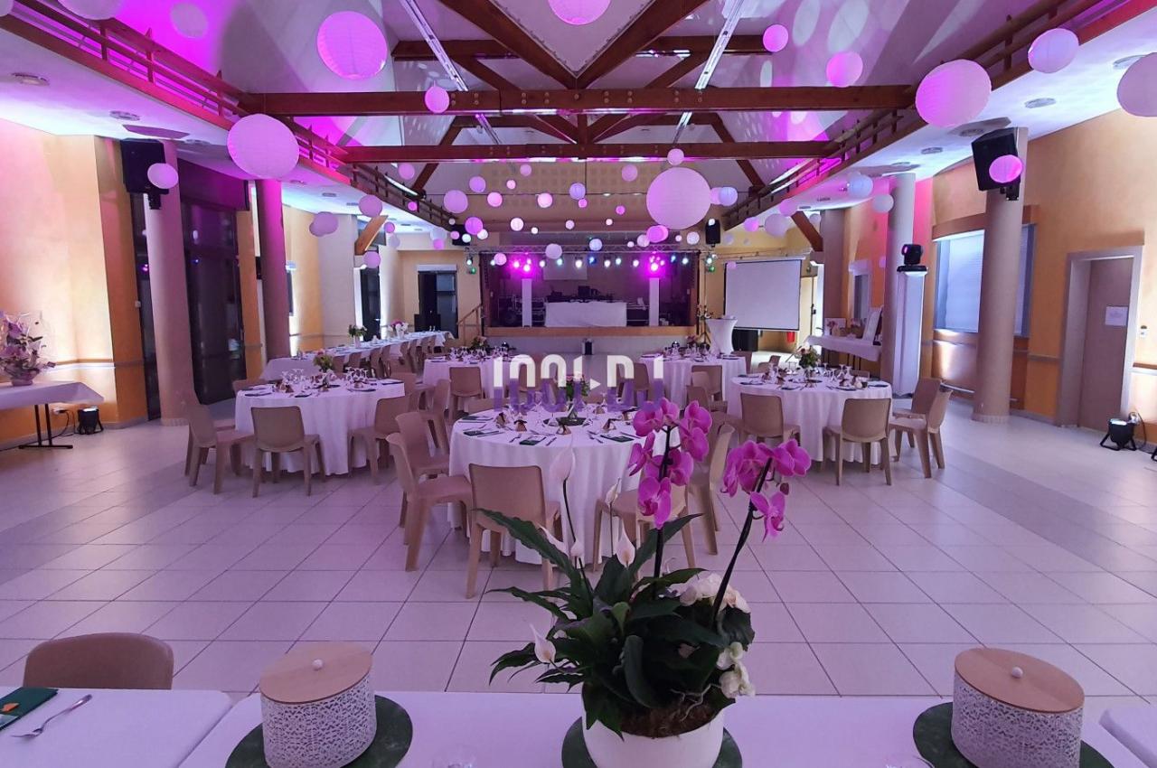 Salle de réception décorée avec des tables dressées, éclairage rose et lanternes suspendues au plafond.