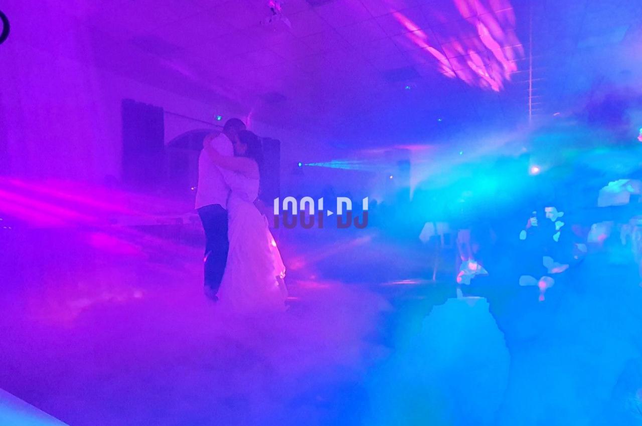 Un couple danse dans une salle éclairée par des lumières colorées et entourée de fumée.
