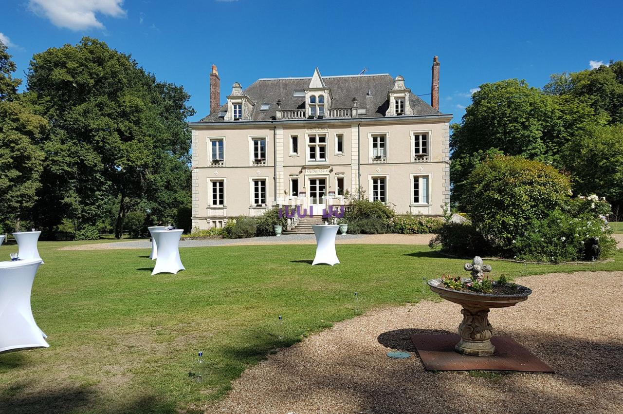 Manoir entouré de verdure avec des tables hautes blanches disposées sur une pelouse ensoleillée.