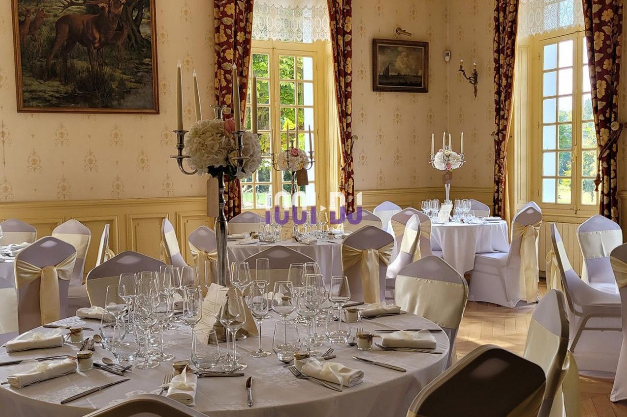 Salle de réception élégante avec tables rondes dressées, nappes blanches et décorations florales, éclairée par la lumière…