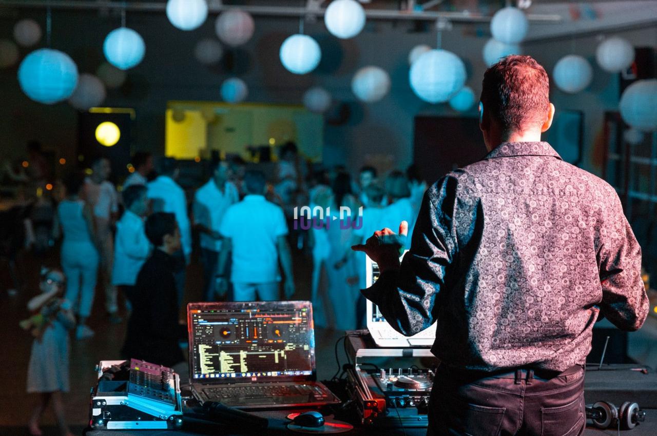 Un DJ mixe de la musique sur scène face à une foule dans une salle décorée de lanternes suspendues.