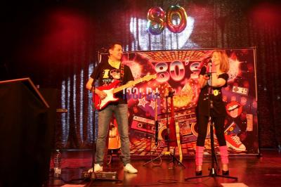 Salle de réception en pierre avec invités assis et debout, décorations florales suspendues et ambiance chaleureuse.