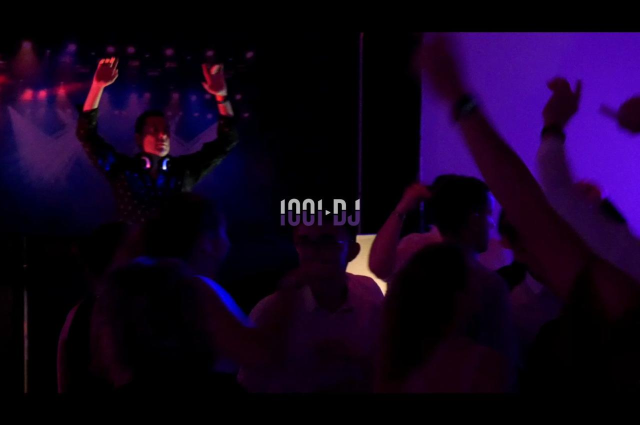 Un DJ anime une soirée dansante avec des lumières colorées et une foule en mouvement.