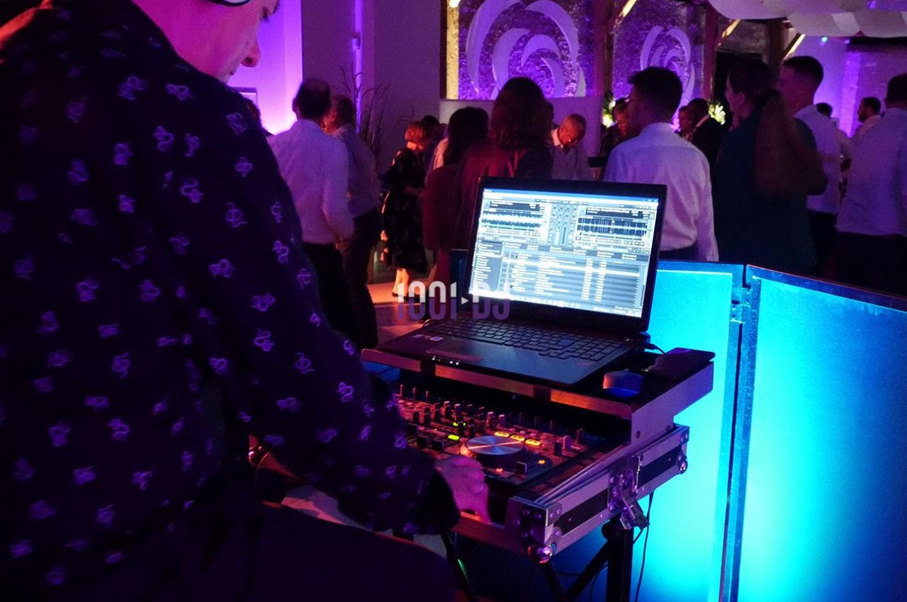 Un DJ mixe de la musique sur une console avec un ordinateur portable lors d'une soirée dansante éclairée par des lumières…