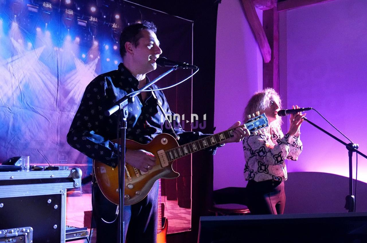 Un guitariste et une chanteuse se produisent sur scène sous des éclairages colorés dans une ambiance musicale.