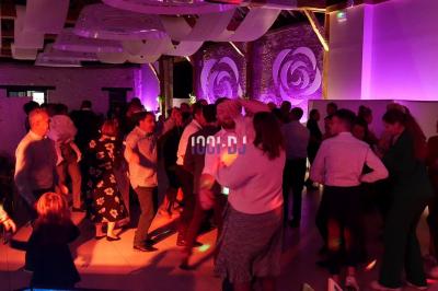 Salle de réception en pierre avec invités assis et debout, décorations florales suspendues et ambiance chaleureuse.