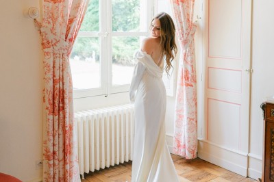 Château éclairé de nuit avec des lumières colorées, entouré de buissons et de tentes blanches sous un ciel nuageux.
