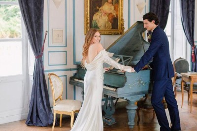 Château éclairé de nuit avec des lumières colorées, entouré de buissons et de tentes blanches sous un ciel nuageux.