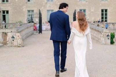 Château éclairé de nuit avec des lumières colorées, entouré de buissons et de tentes blanches sous un ciel nuageux.
