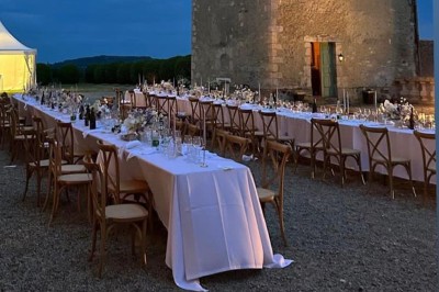 Château éclairé de nuit avec des lumières colorées, entouré de buissons et de tentes blanches sous un ciel nuageux.