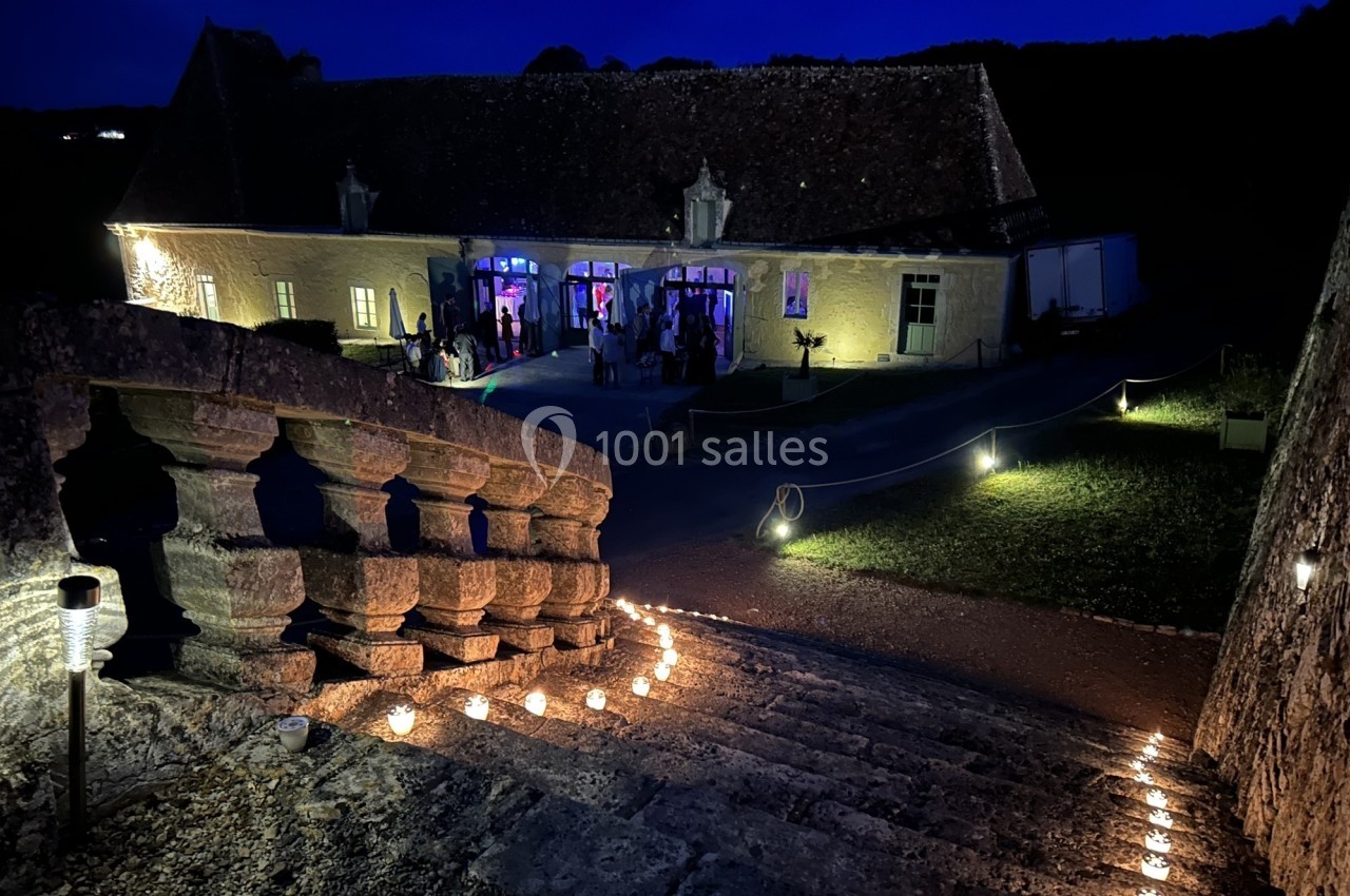 Escalier en pierre illuminé menant à une bâtisse éclairée de nuit, avec des invités visibles à l'intérieur.