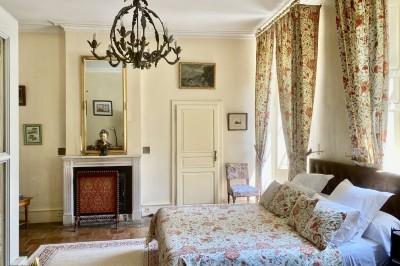 Château éclairé de nuit avec des lumières colorées, entouré de buissons et de tentes blanches sous un ciel nuageux.