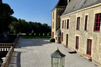 Château éclairé de nuit avec des lumières colorées, entouré de buissons et de tentes blanches sous un ciel nuageux.