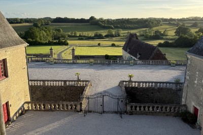 Château éclairé de nuit avec des lumières colorées, entouré de buissons et de tentes blanches sous un ciel nuageux.