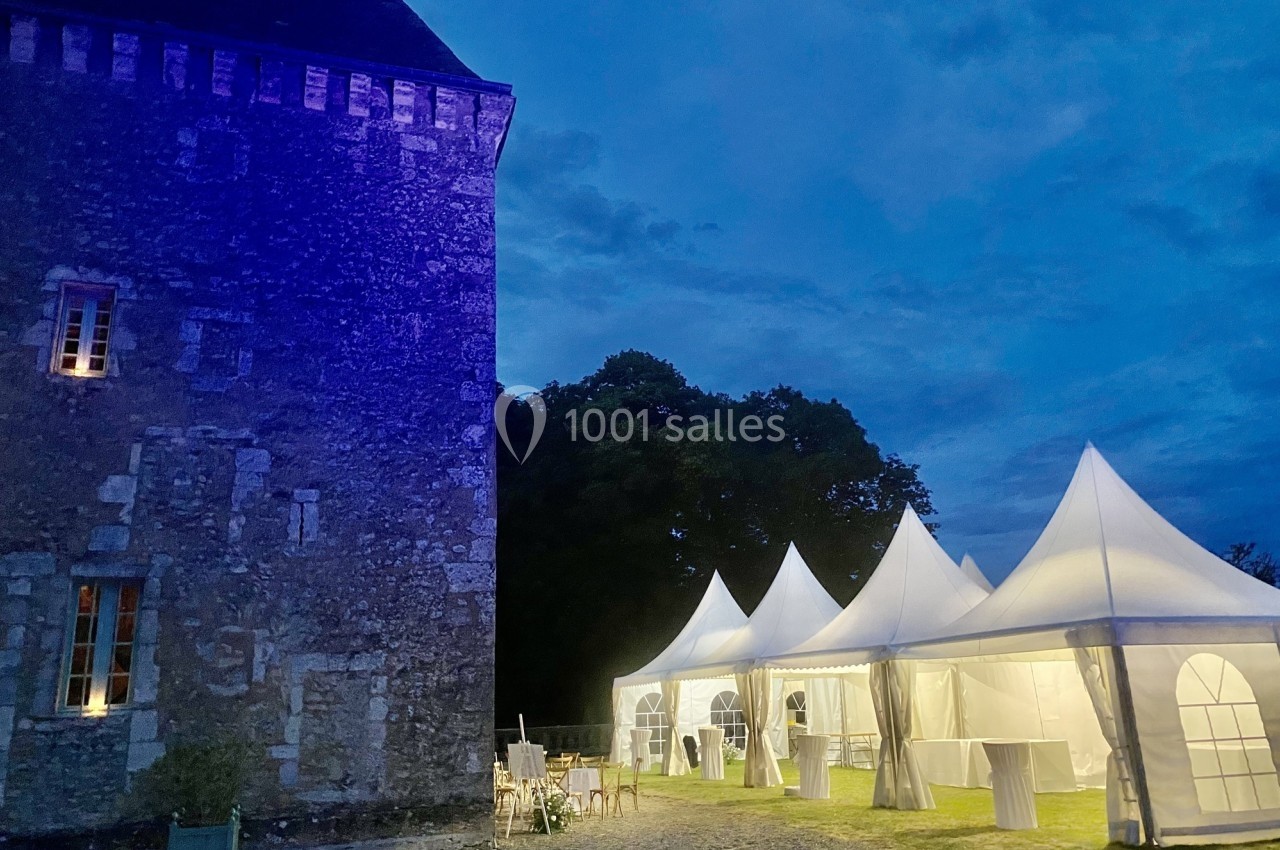 Tentes blanches éclairées installées près d'un bâtiment en pierre ancienne, dans un cadre extérieur nocturne.