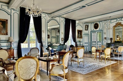Château éclairé de nuit avec des lumières colorées, entouré de buissons et de tentes blanches sous un ciel nuageux.