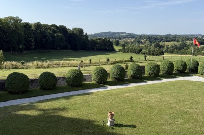 Château éclairé de nuit avec des lumières colorées, entouré de buissons et de tentes blanches sous un ciel nuageux.