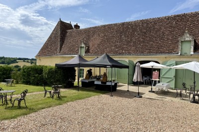 Château éclairé de nuit avec des lumières colorées, entouré de buissons et de tentes blanches sous un ciel nuageux.