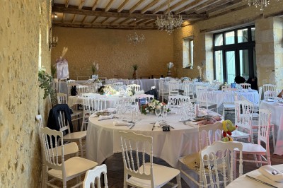 Château éclairé de nuit avec des lumières colorées, entouré de buissons et de tentes blanches sous un ciel nuageux.