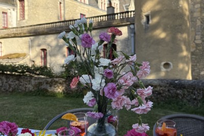 Château éclairé de nuit avec des lumières colorées, entouré de buissons et de tentes blanches sous un ciel nuageux.