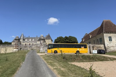 Château éclairé de nuit avec des lumières colorées, entouré de buissons et de tentes blanches sous un ciel nuageux.