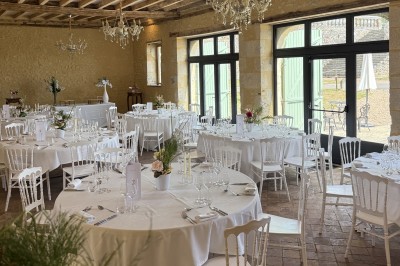 Château éclairé de nuit avec des lumières colorées, entouré de buissons et de tentes blanches sous un ciel nuageux.