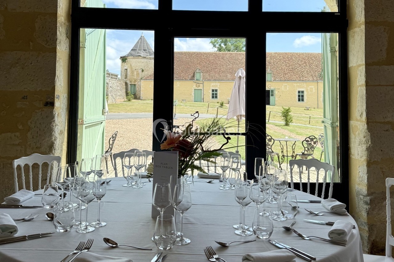 Table dressée avec vaisselle élégante devant des portes vitrées ouvertes sur une cour pavée et des bâtiments anciens.