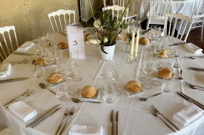 Château éclairé de nuit avec des lumières colorées, entouré de buissons et de tentes blanches sous un ciel nuageux.