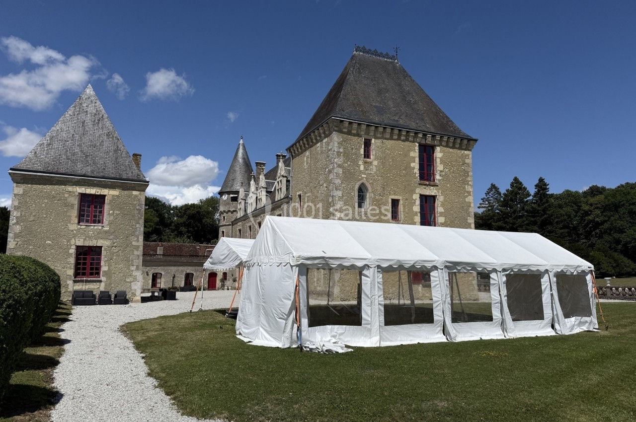 Tente blanche installée sur une pelouse devant un château en pierre avec ciel bleu en arrière-plan.