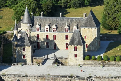 Château éclairé de nuit avec des lumières colorées, entouré de buissons et de tentes blanches sous un ciel nuageux.