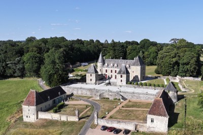 Château éclairé de nuit avec des lumières colorées, entouré de buissons et de tentes blanches sous un ciel nuageux.