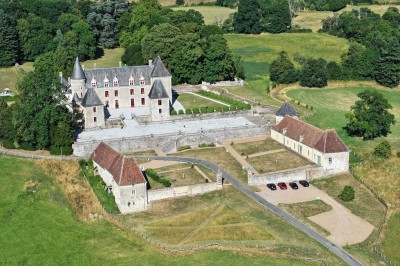 Château éclairé de nuit avec des lumières colorées, entouré de buissons et de tentes blanches sous un ciel nuageux.