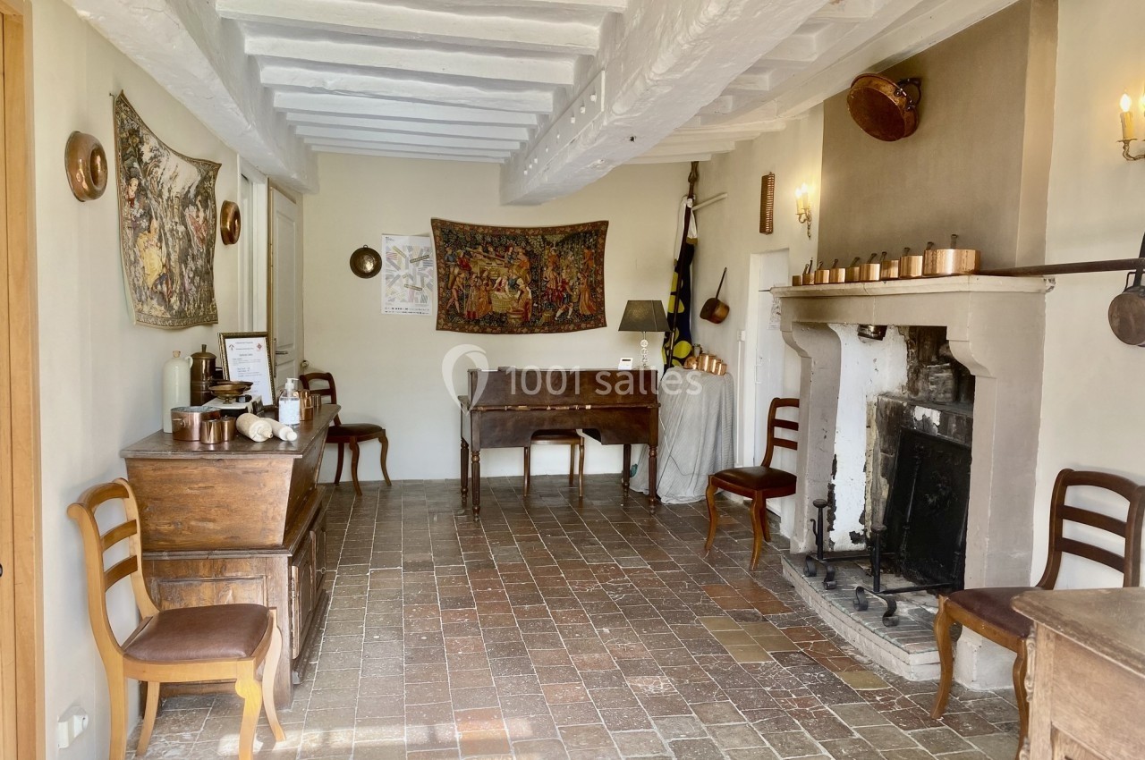 Salle ancienne avec cheminée, meubles en bois, tapisseries murales et sol en carreaux de terre cuite.