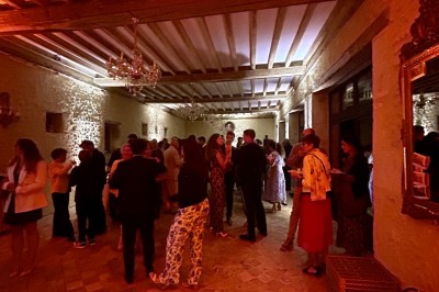 Château éclairé de nuit avec des lumières colorées, entouré de buissons et de tentes blanches sous un ciel nuageux.