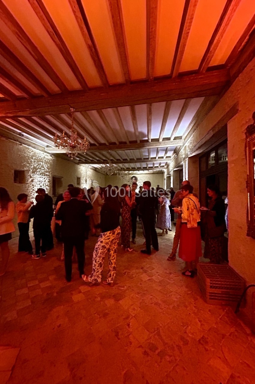 Groupe de personnes discutant dans une grande salle éclairée par une lumière chaude, avec plafond à poutres apparentes.